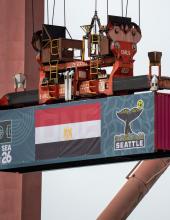 A shipping container with an Egypt flag banner hangs from a crane at Terminal 46 in Seattle.