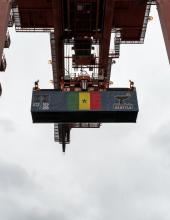A shipping container with a Senegal flag banner hangs from a crane at Terminal 46 in Seattle.