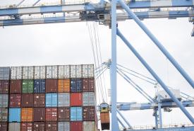 Shot of a suspended crane moving containers off of a ship in front of a terminal.